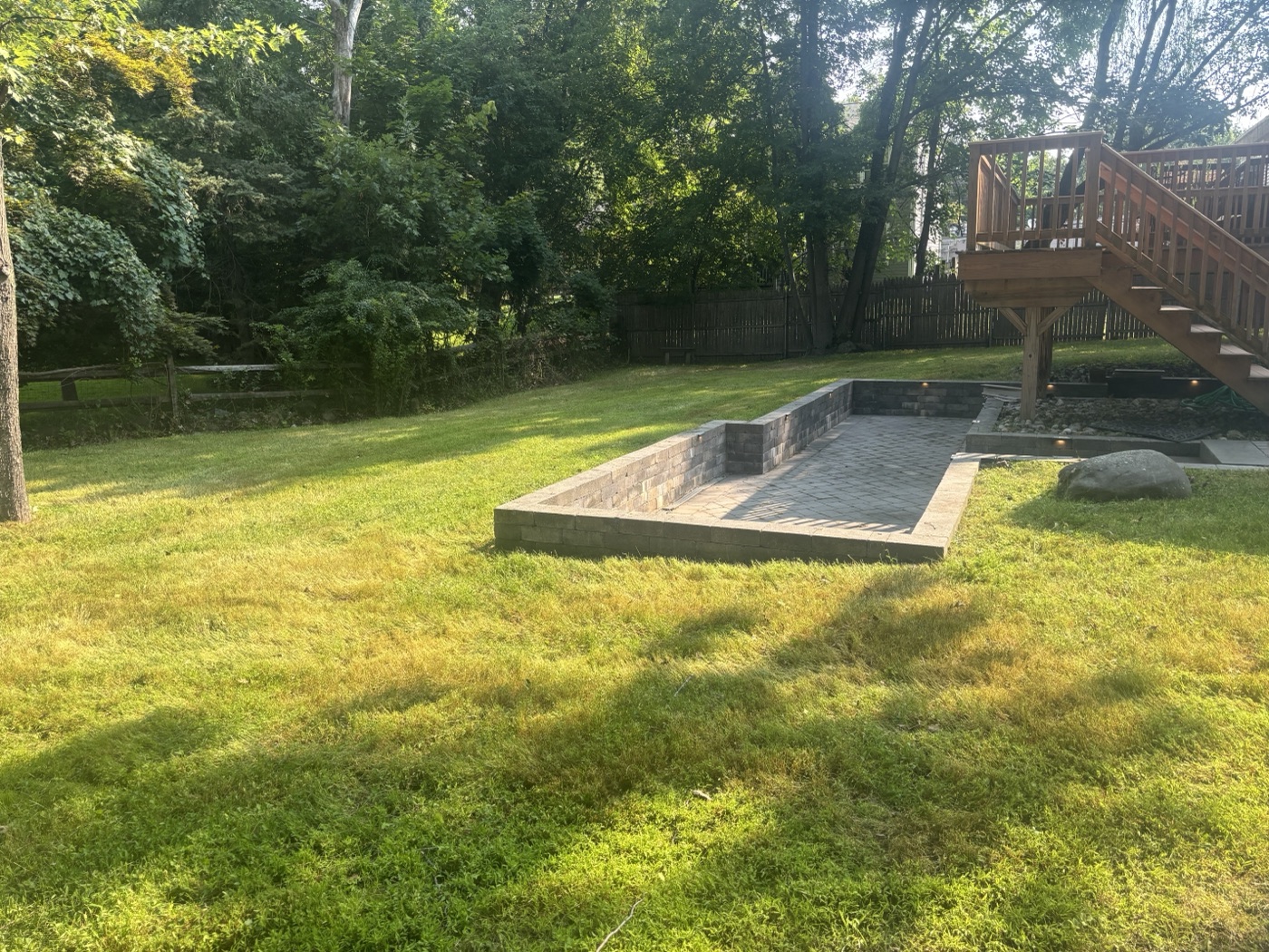 After: raised paver patio with retaining wall beside deck
